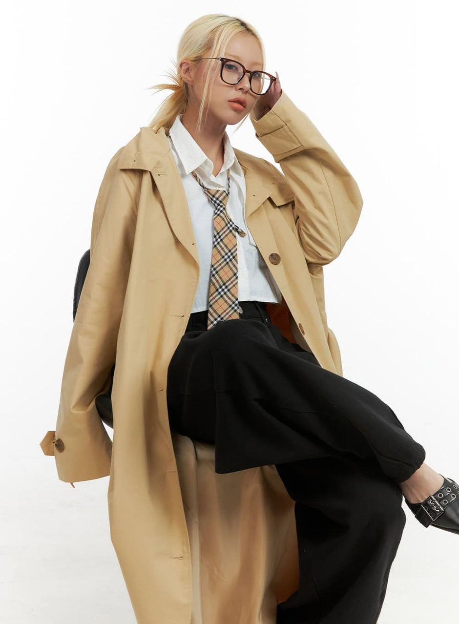 a woman in a trench coat and tie sitting on a chair